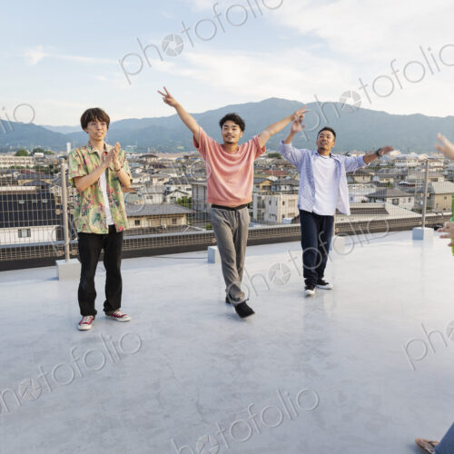Group of young Japanese men and women dancing on a rooftop in an urban setting. Group of young Japanese men and women dancing on a rooftop in an urban setting.