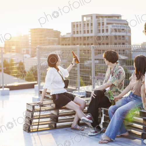 Group of young Japanese men and women sitting on a rooftop in an urban setting.