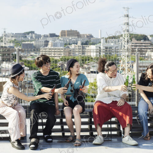 Group of young Japanese men and women sitting on a rooftop in an urban setting,… Group of young Japanese men and women sitting on a rooftop in an urban setting,…