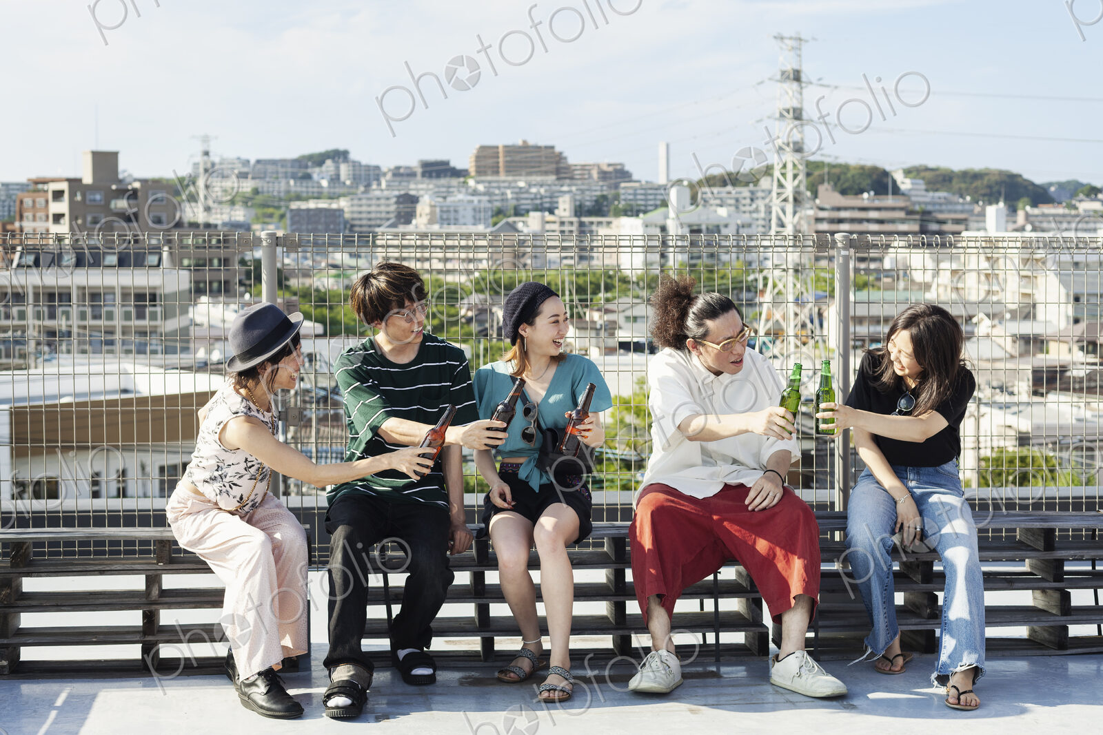 Group of young Japanese men and women sitting on a rooftop in an urban setting,…