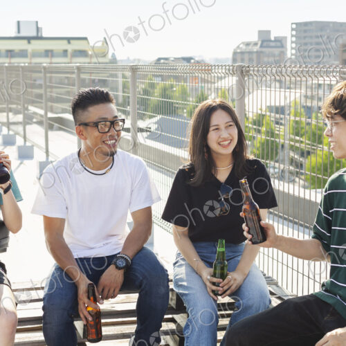Group of young Japanese men and women sitting on a rooftop in an urban setting,… Group of young Japanese men and women sitting on a rooftop in an urban setting,…