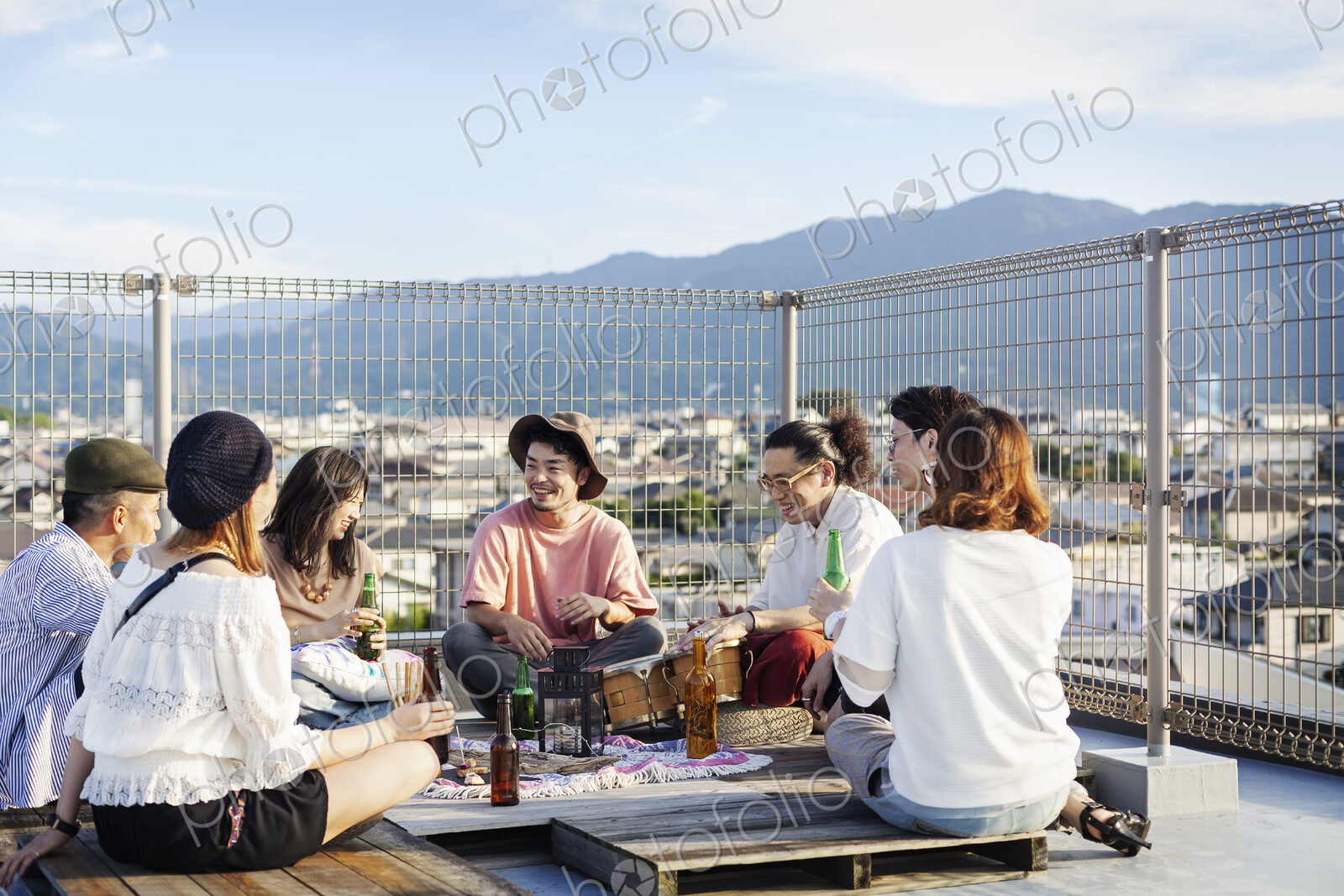Group of young Japanese men and women sitting on a rooftop in an urban setting,…