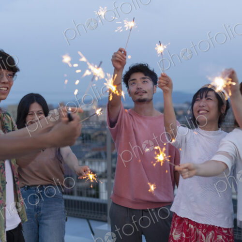 Group of young Japanese men and women with sparklers on a rooftop in an urban setting. Group of young Japanese men and women with sparklers on a rooftop in an urban setting.