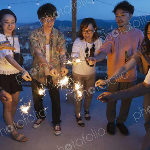 Group of young Japanese men and women with sparklers on a rooftop in an urban setting. Group of young Japanese men and women with sparklers on a rooftop in an urban setting.