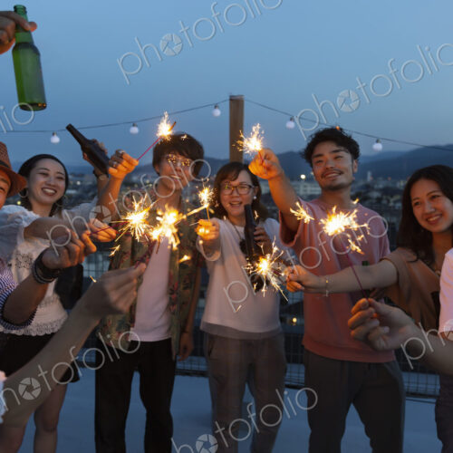 Group of young Japanese men and women with sparklers on a rooftop in an urban setting. Group of young Japanese men and women with sparklers on a rooftop in an urban setting.