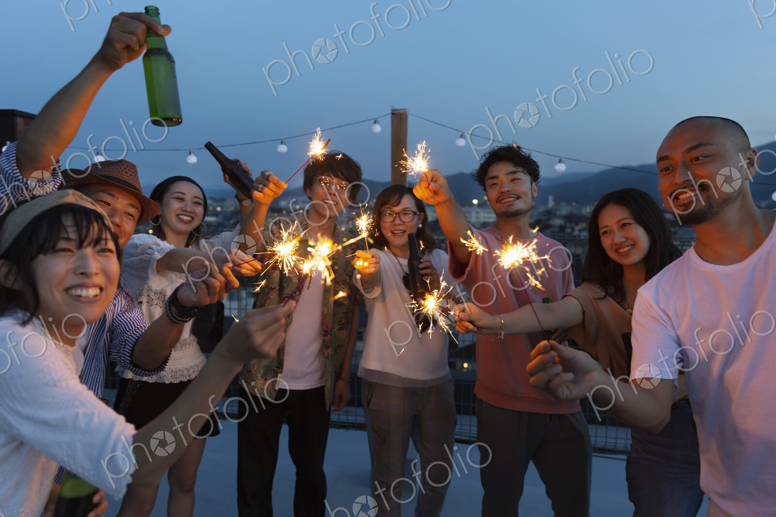 Group of young Japanese men and women with sparklers on a rooftop in an urban setting.