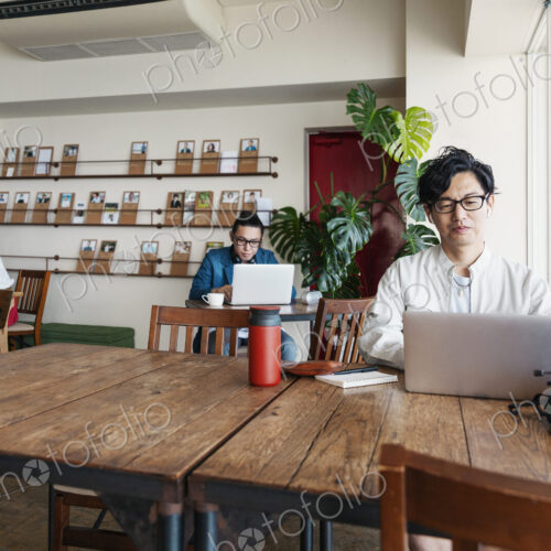Group of young Japanese professionals working on laptop computers in a co-working space.