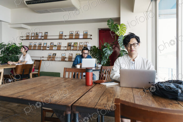 Group of young Japanese professionals working on laptop computers in a co-working space.