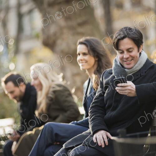 Group on bench in urban park using smartphones Group on bench in urban park using smartphones