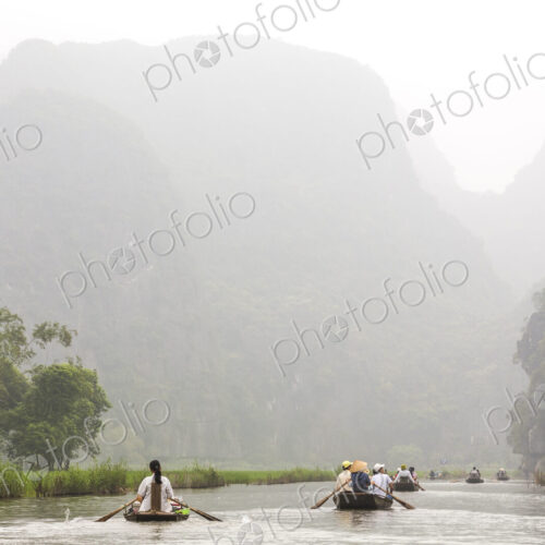 Groups of people in rowboats on a river, mountains in the background.