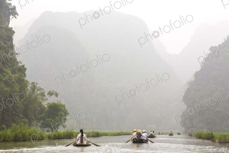 Groups of people in rowboats on a river, mountains in the background.