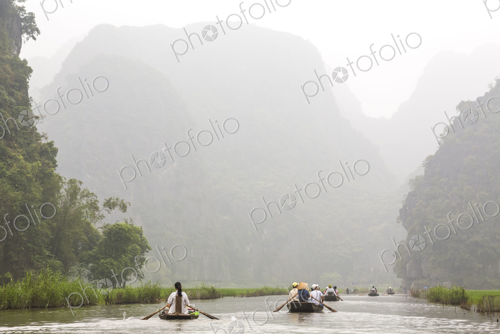 Groups of people in rowboats on a river, mountains in the background.