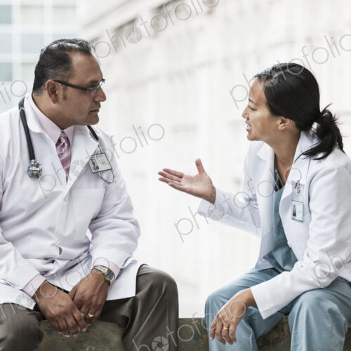 HIspanic man and asian woman doctors conferring over a case in a hospital. HIspanic man and asian woman doctors conferring over a case in a hospital.
