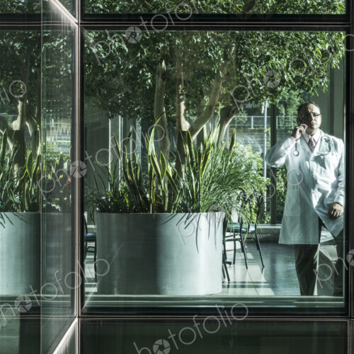 HIspanic man doctor on phone in a hospital lobby.