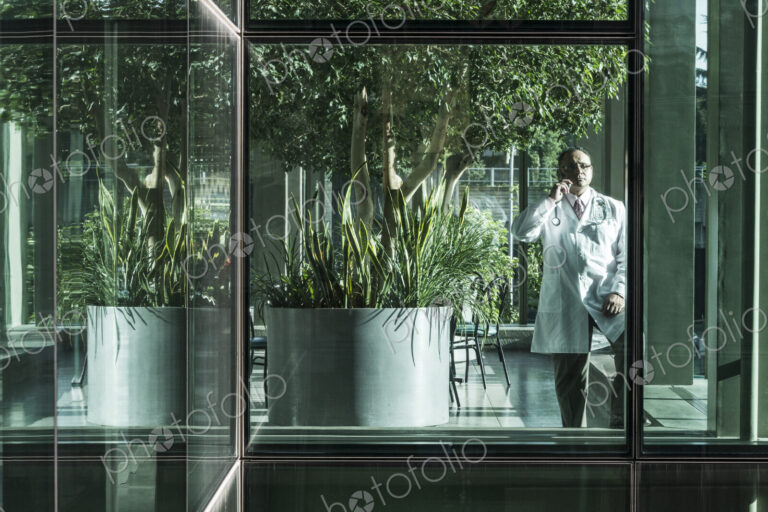 HIspanic man doctor on phone in a hospital lobby.