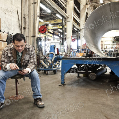 HIspanic man factory worker checking a part inventory on his cell phone in a sheet…