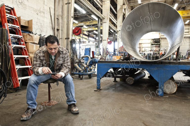 HIspanic man factory worker checking a part inventory on his cell phone in a sheet…
