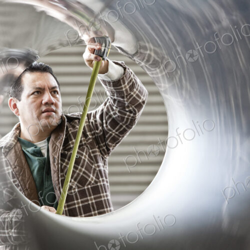 HIspanic man factory worker measuring diameter of pipe in a sheet metal factory.
