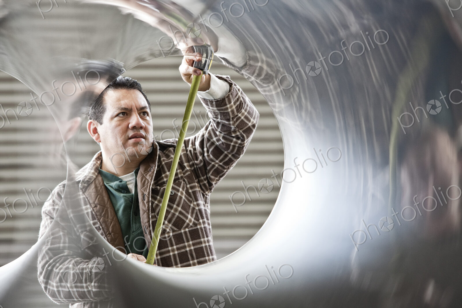 HIspanic man factory worker measuring diameter of pipe in a sheet metal factory.