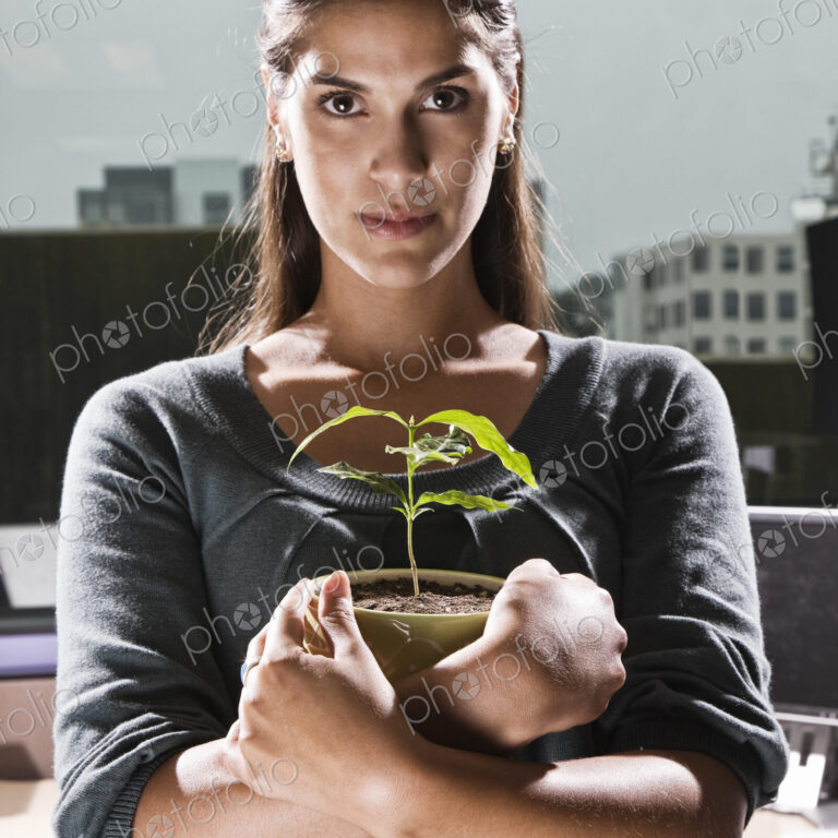 HIspanic woman holding a house plant in an office cubicle.