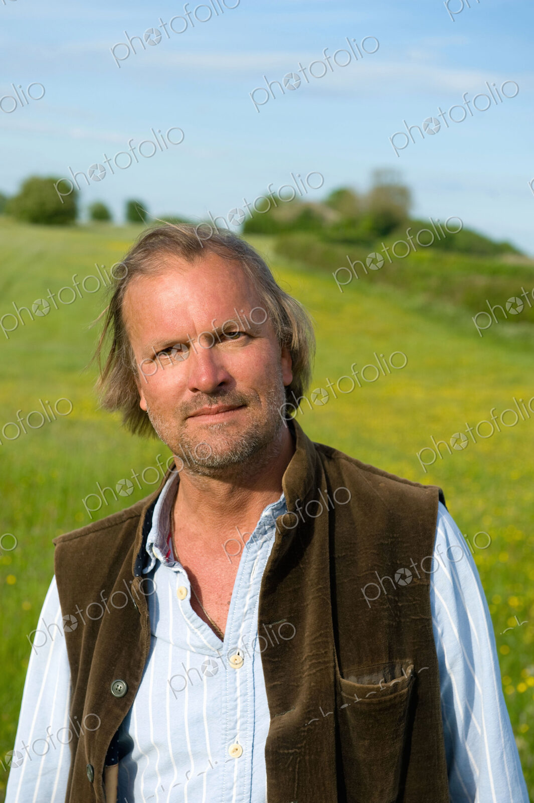 Half length portrait of mature man standing outdoors on a meadow, smiling at camera.