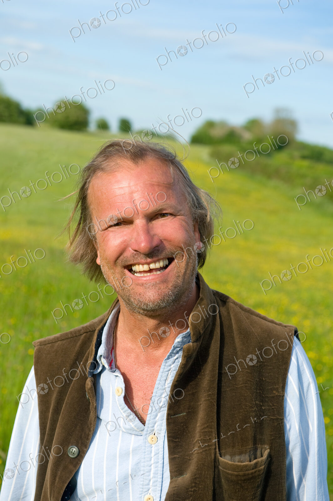 Half length portrait of mature man standing outdoors on a meadow, smiling at camera.