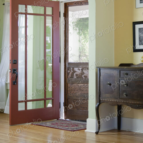 Hallway with wood floor and front door and screen door in a traditional home.