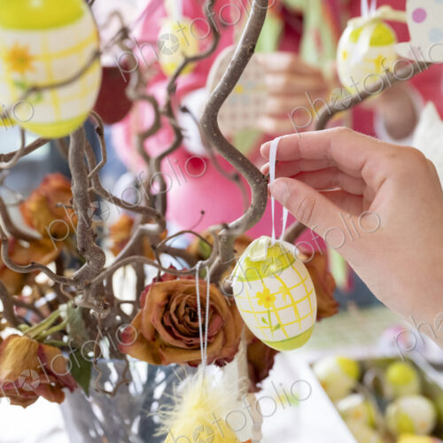 Hand arranging colourful Easter ornaments on brances in vase on kitchen table. Hand arranging colourful Easter ornaments on brances in vase on kitchen table.