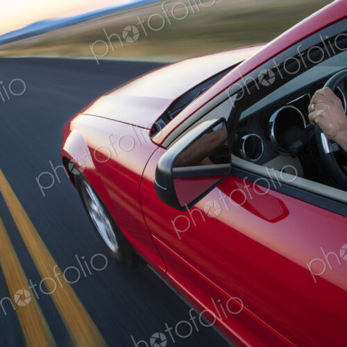 Hand on a steering wheel of a convertible sports car moving on the highway.
