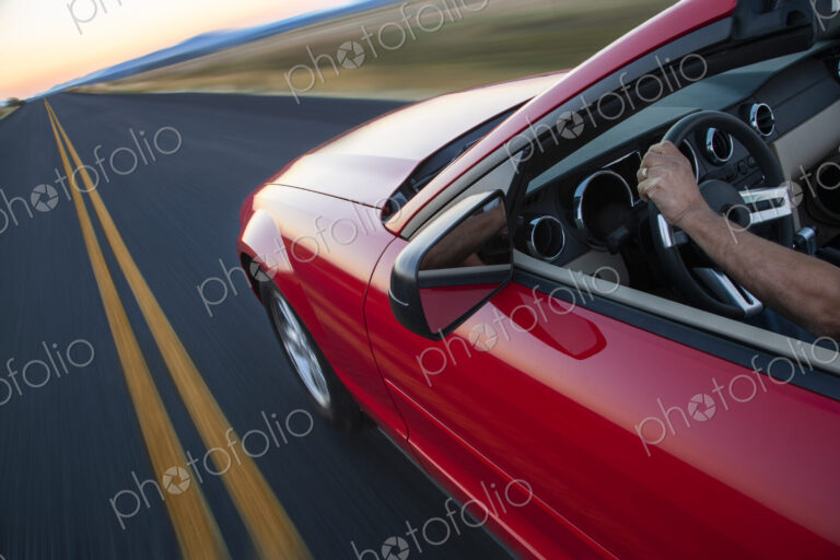 Hand on a steering wheel of a convertible sports car moving on the highway.