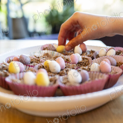 Hand putting decorations on to Easter cup cakes in dish on kitchen table. Hand putting decorations on to Easter cup cakes in dish on kitchen table.