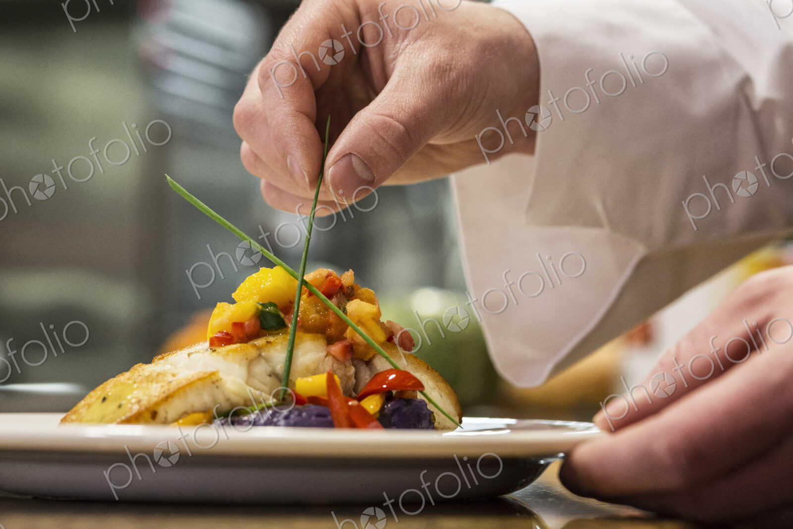 Hands of a chef dressing a plate of fish in a commercial kitchen,