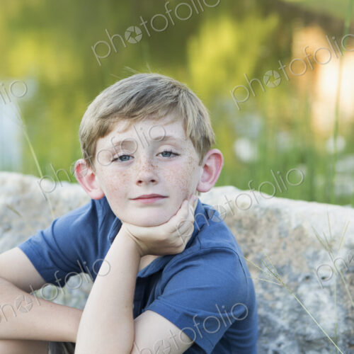 Head and shoulders portrait of a young boy sitting with his chin resting on his hand.