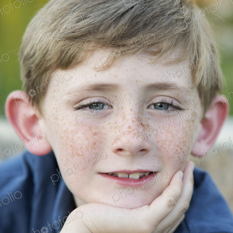 Head and shoulders portrait of a young boy sitting with his chin resting on his hand.