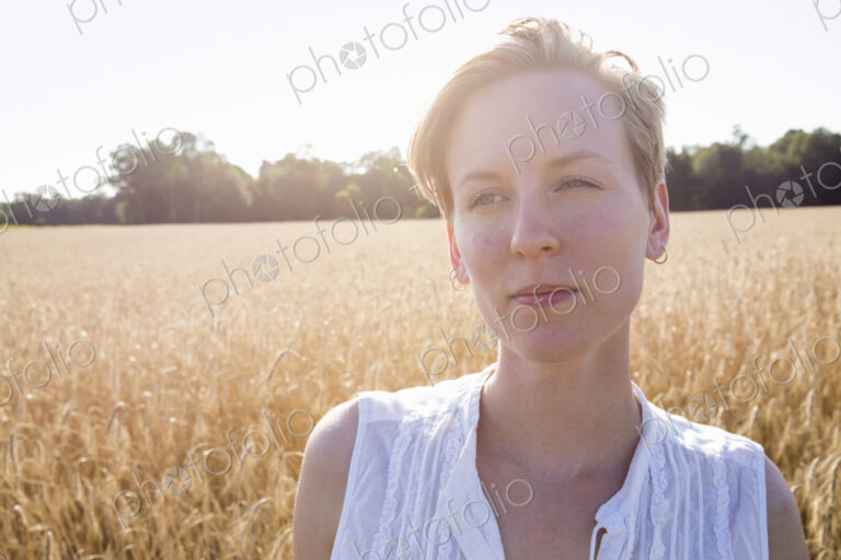 Head and shoulders portrait of a young woman standing in a cornfield.