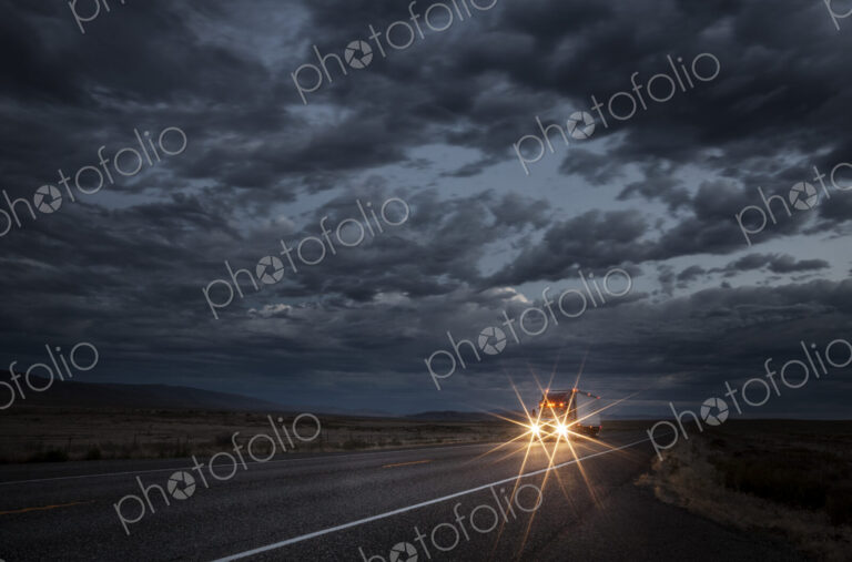Headlights of a commercial truck on a highway late in the day.