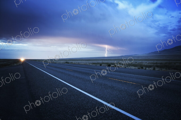 Headlights of a commercial truck on a highway late in the day.