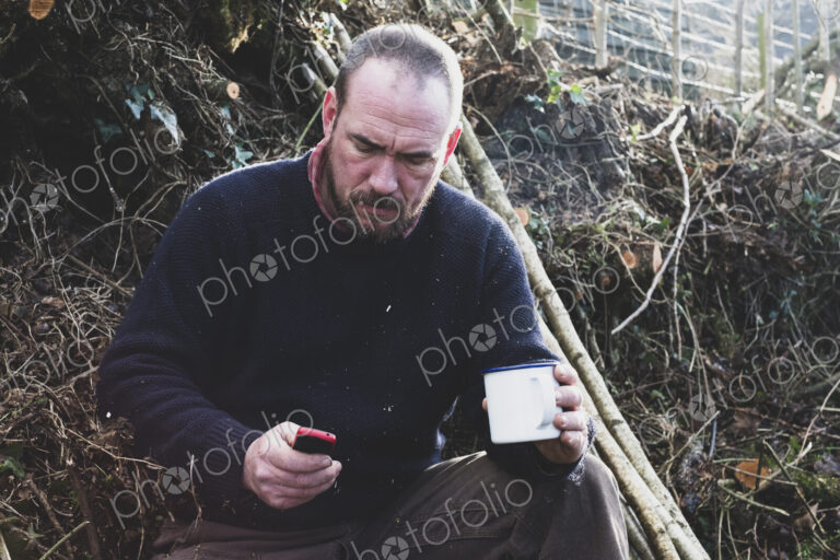 Hedge layer on a tea break checking his mobile phone.