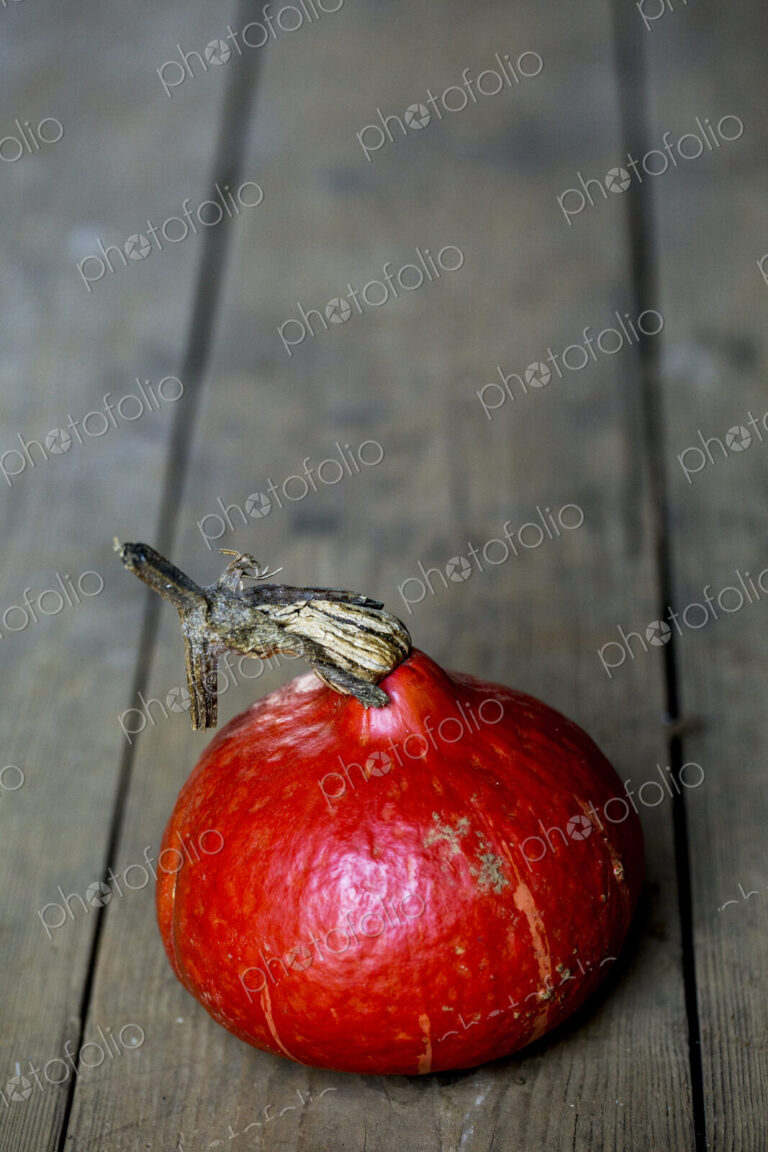High angle close up of a Red Kuri pumpkin on rustic wooden table.