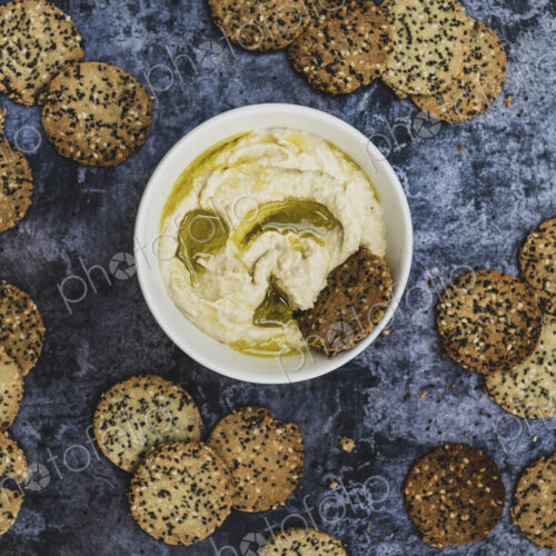 High angle close up of a bowl of hummus and freshly baked seeded crackers.