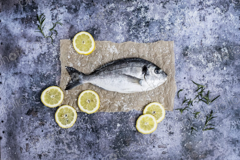 High angle close up of a fresh sea bream, slices of lemon and fresh rosemary.