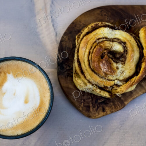 High angle close up of a freshly baked cinnamon bun and a cup of cappuccino. High angle close up of a freshly baked cinnamon bun and a cup of cappuccino.