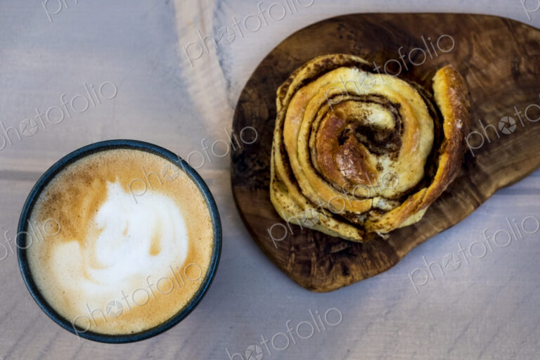 High angle close up of a freshly baked cinnamon bun and a cup of cappuccino.