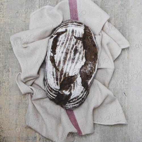 High angle close up of a freshly baked loaf of brown bread on tea towel. High angle close up of a freshly baked loaf of brown bread on tea towel.