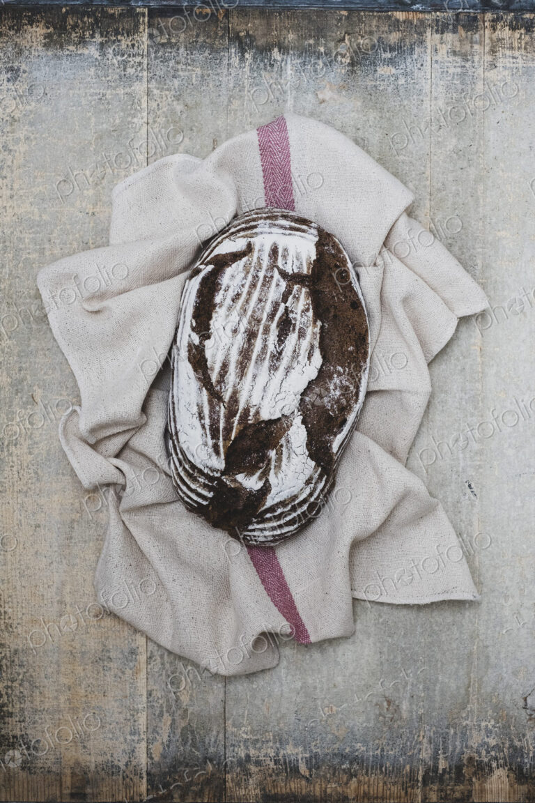 High angle close up of a freshly baked loaf of brown bread on tea towel.