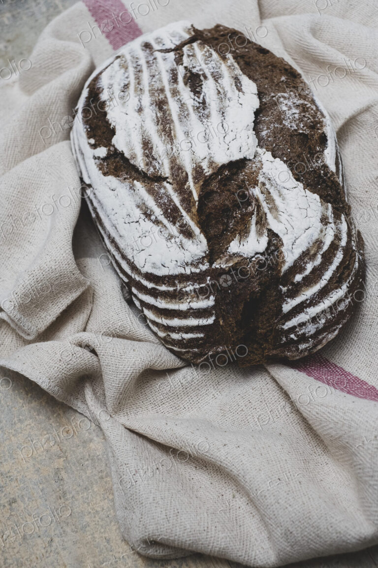 High angle close up of a freshly baked loaf of brown bread on tea towel.