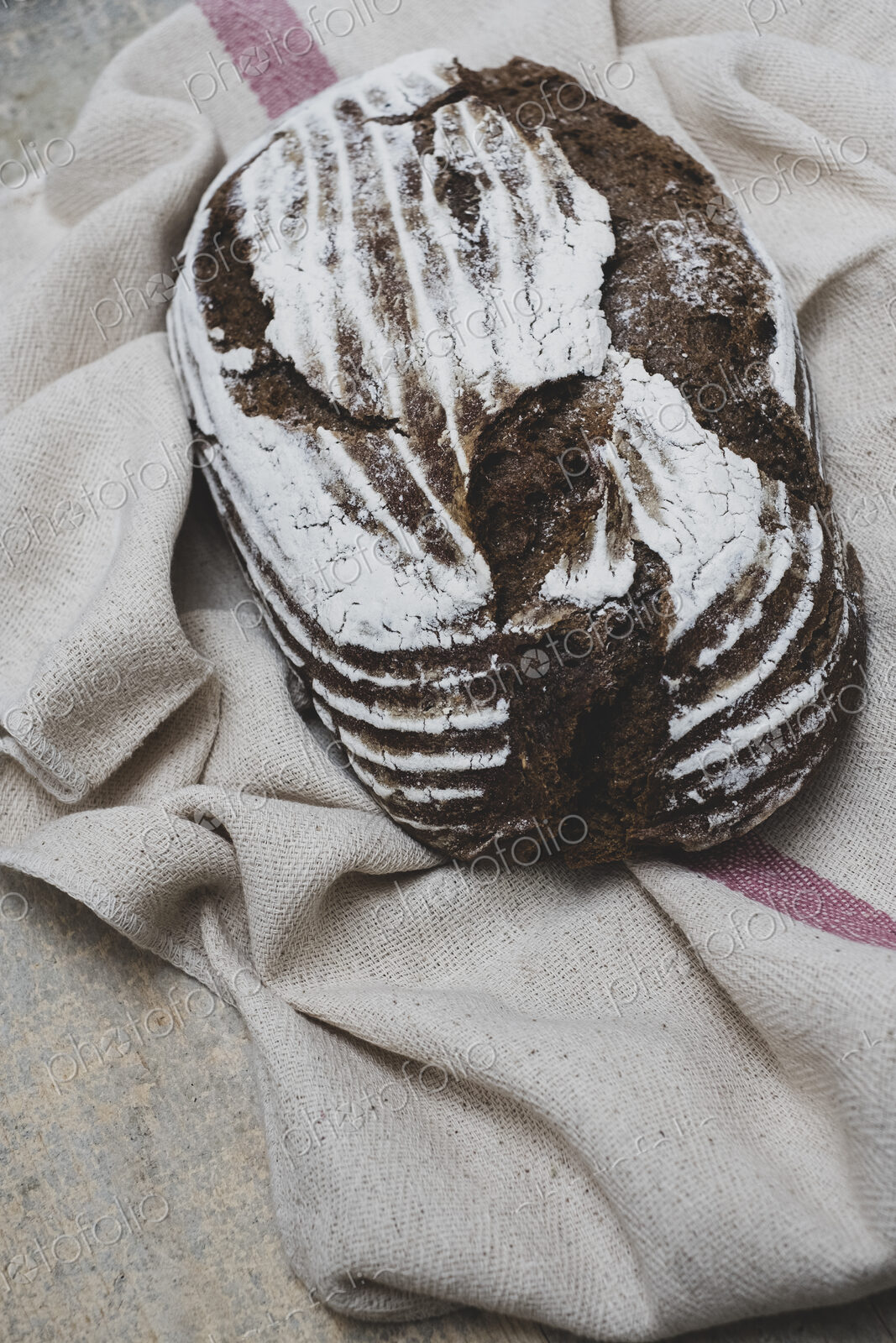 High angle close up of a freshly baked loaf of brown bread on tea towel.