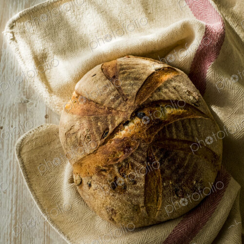 High angle close up of a freshly baked round loaf of bread on tea towel. High angle close up of a freshly baked round loaf of bread on tea towel.