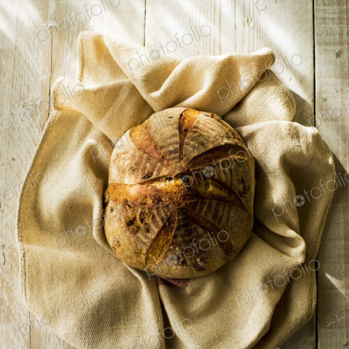 High angle close up of a freshly baked round loaf of bread on tea towel. High angle close up of a freshly baked round loaf of bread on tea towel.