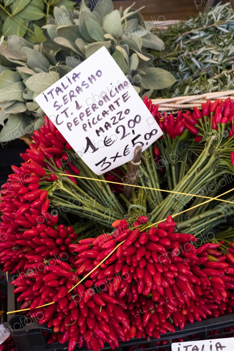 High angle close up of a large bunch of fresh red chillies at an Italian market stall.